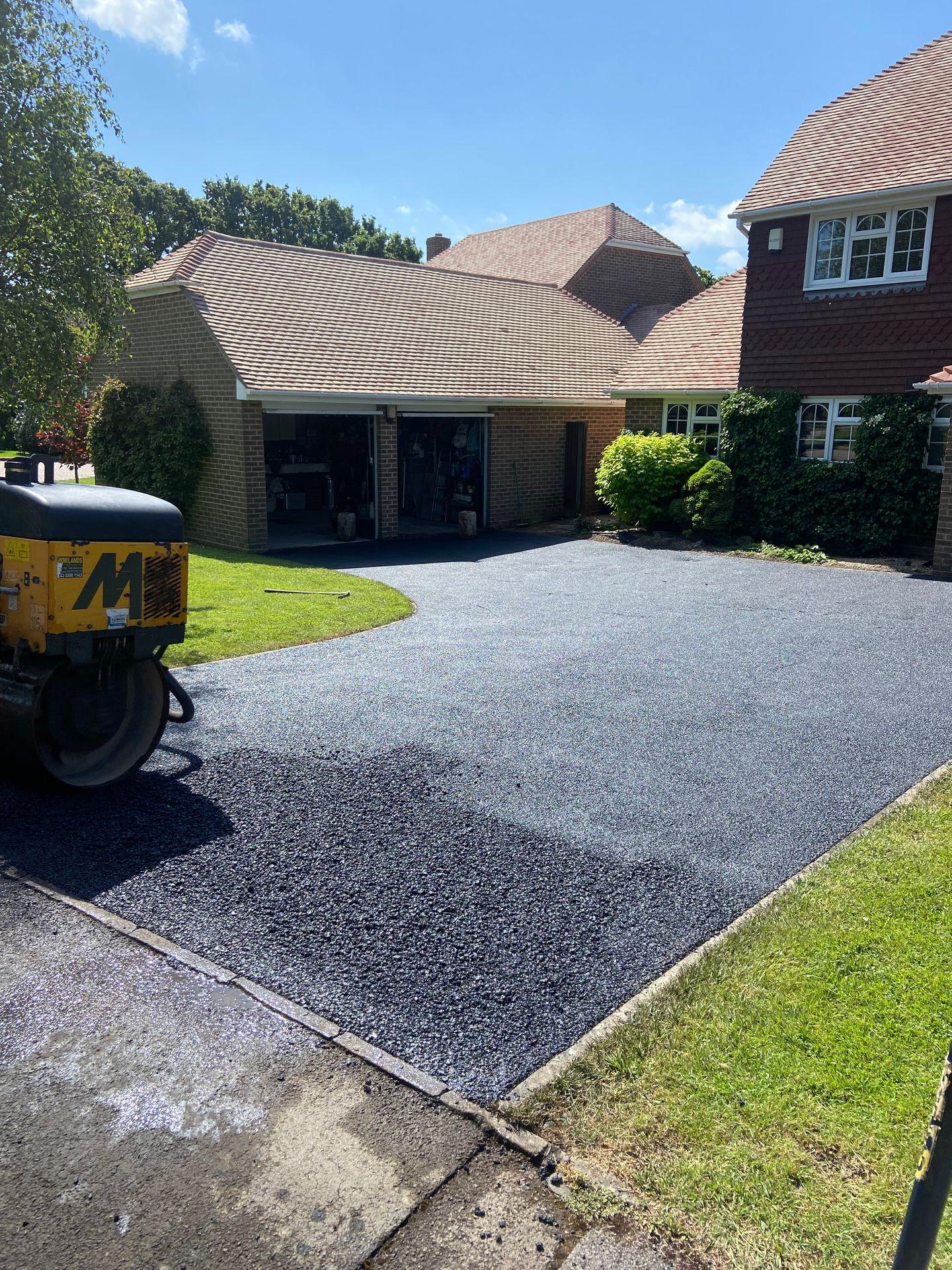 Freshly paved driveway in front of a suburban house with open garage and parked construction vehicle.